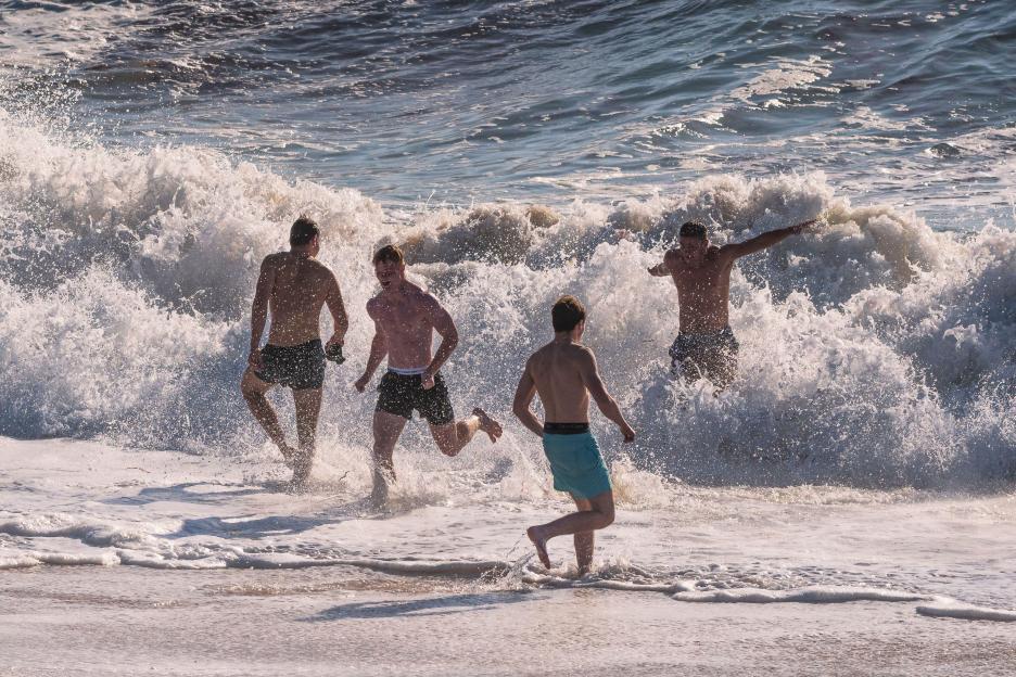 Four men running into the ocean waves.
