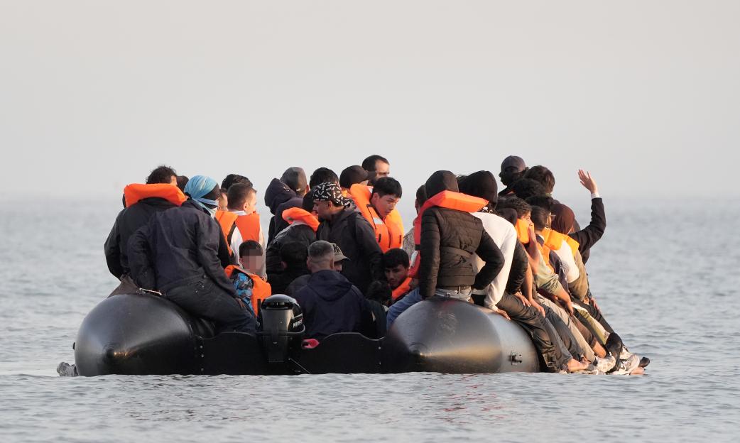 Migrants in a small boat at sea. Children's faces are pixelated.