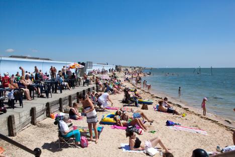 Crowded beach scene with people sunbathing and swimming.