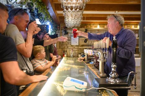 Man pouring a pint of beer behind a bar, surrounded by photographers.