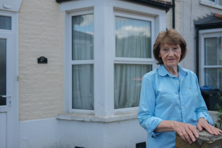 Sue standing outside a house, questioning a will.