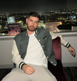 Man sitting in a chair in front of a window with a nighttime view of Los Angeles.