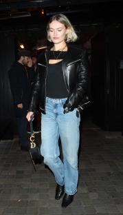 Woman in black leather jacket and jeans leaving a building.