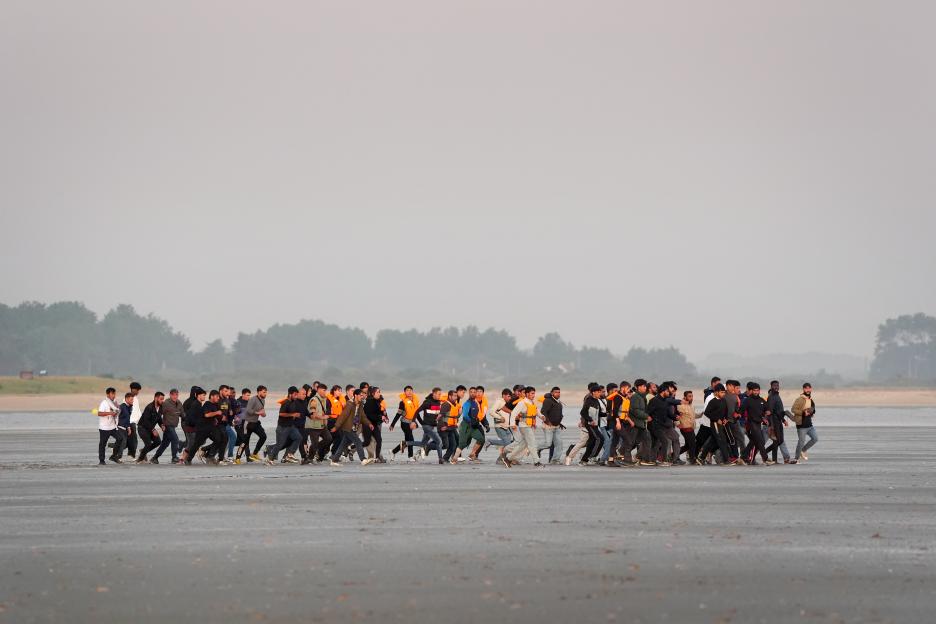 Migrants running across a beach to board a small boat.