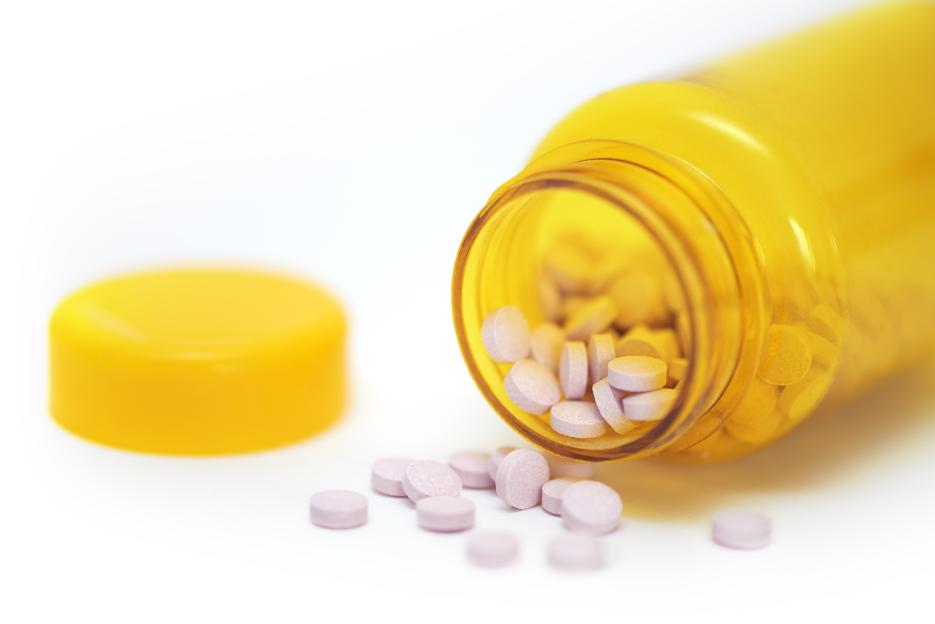 Pink vitamin B-12 pills spilling from a yellow bottle.