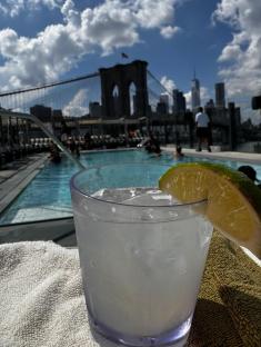 Cocktail by a rooftop pool with the Brooklyn Bridge in the background.