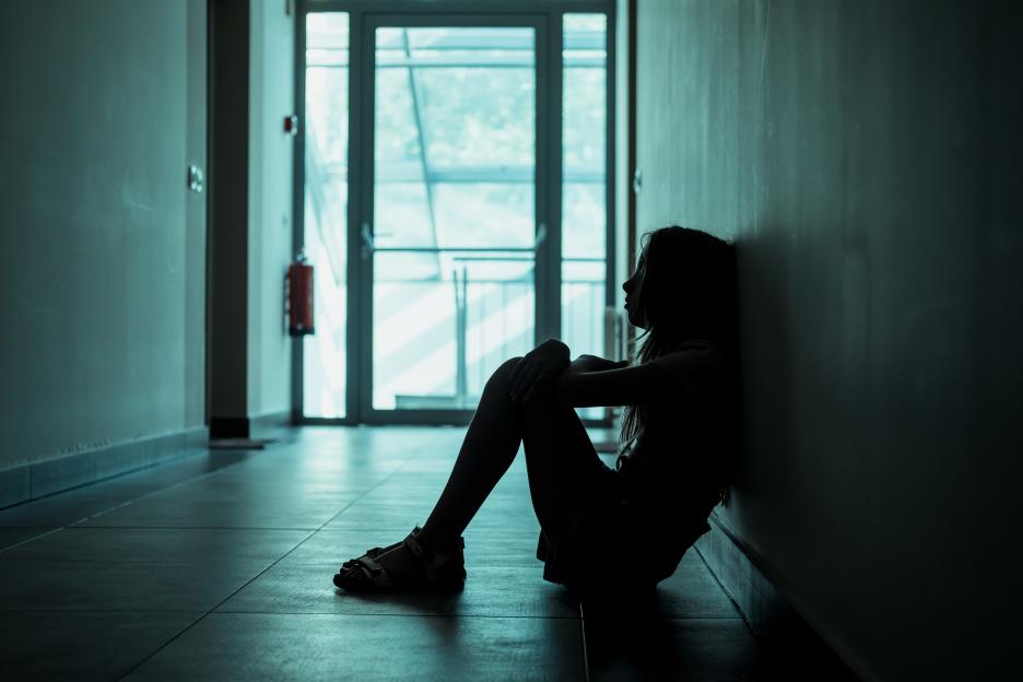 Silhouette of a sad girl sitting on the floor in a hallway.