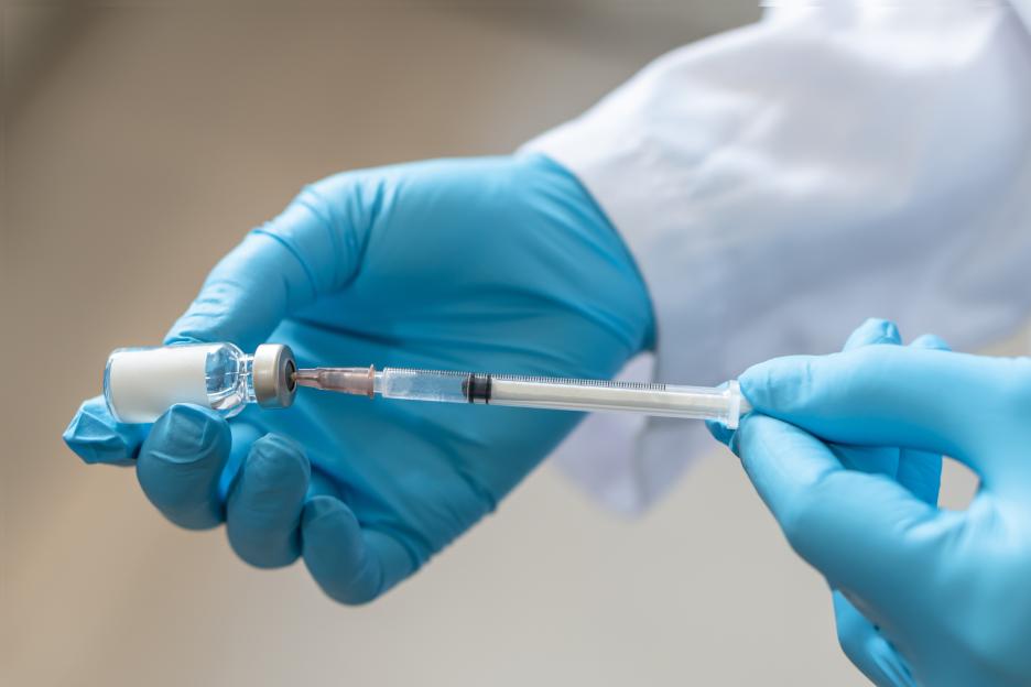 Gloved hands drawing vaccine into a syringe.