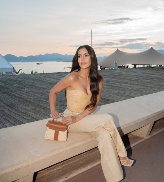 Woman in a beige outfit sitting on a bench by the sea.