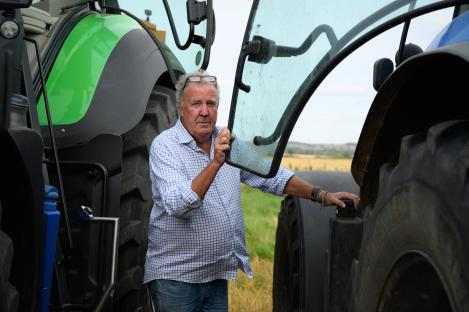 Jeremy Clarkson standing by tractors on a farm.