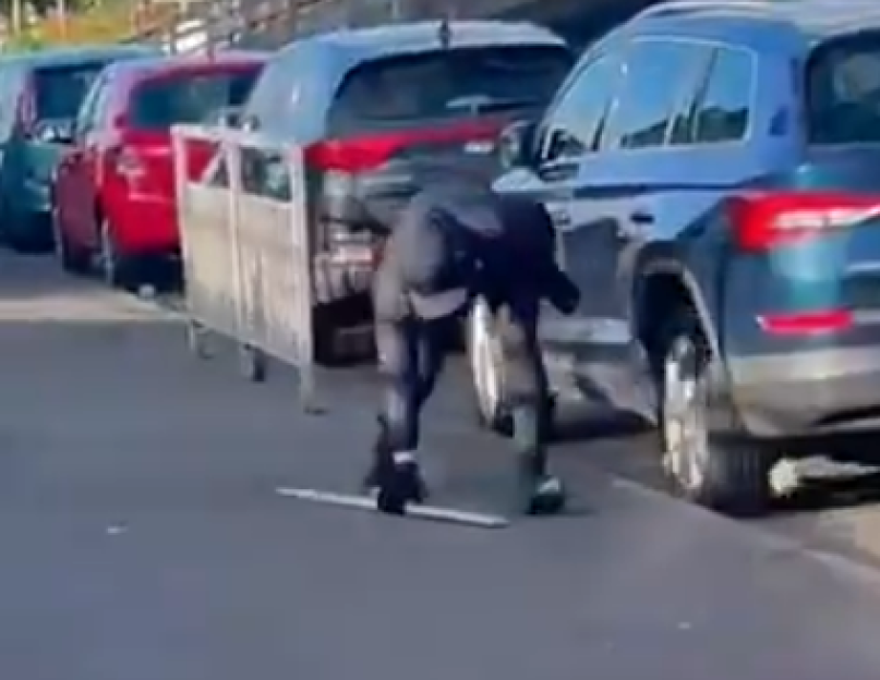 Person crouching near a metal fence beside parked cars.
