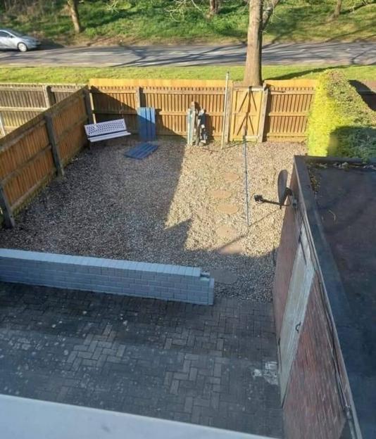 Photo of a small, gravel garden with a wooden fence and brick wall.