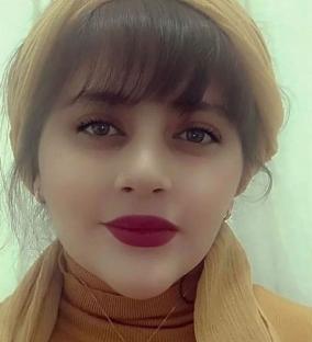 Portrait of a young woman wearing a mustard-colored headscarf and turtleneck.