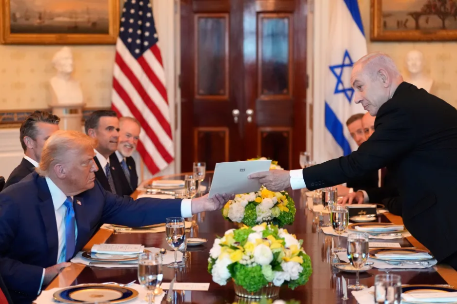 Donald Trump and Benjamin Netanyahu exchanging a document at a table.