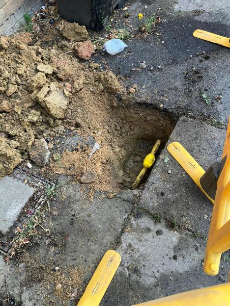 Exposed gas pipe in a dug-up section of pavement.