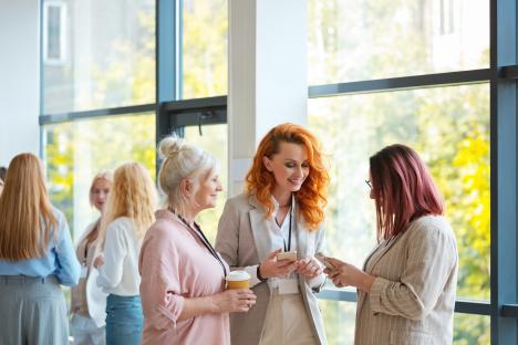 Three businesswomen share a smartphone during a coffee break.