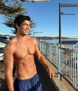 Shirtless man smiling near a beach.