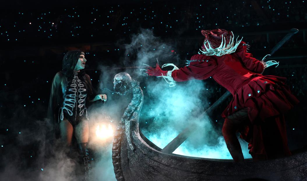 Lady Gaga performing on stage in a boat with a costumed performer.