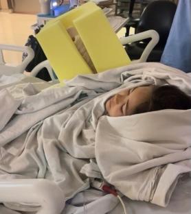 A young girl sleeping under a blanket in a hospital bed.