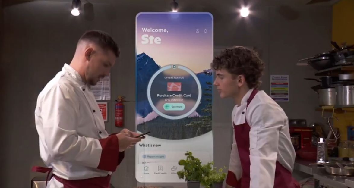 Two chefs in a kitchen looking at a phone displaying a credit card offer.