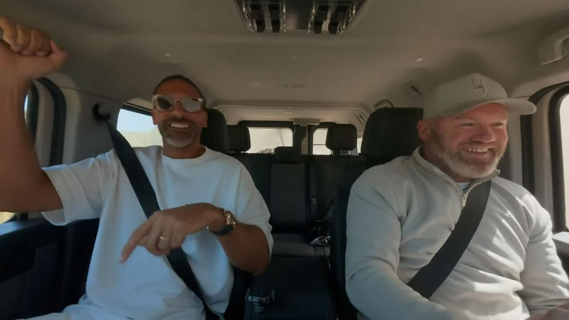 Two men in a car, one with his arm raised.