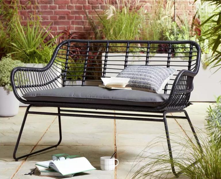 Black wicker patio bench with gray cushions.
