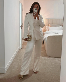Woman in a white pantsuit taking a selfie in a mirror.