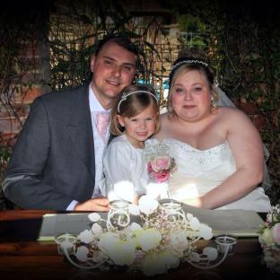 Bride and groom signing their wedding register with their young daughter.