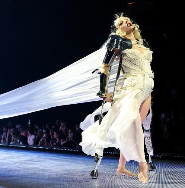 Lady Gaga performing on stage in a white dress and prosthetic leg.
