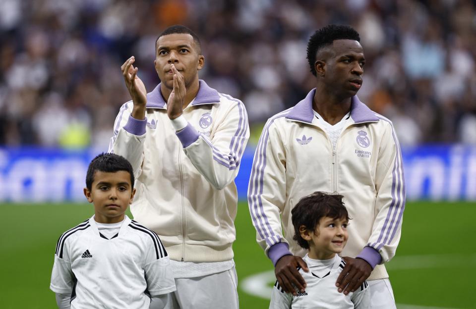 Kylian Mbappé and Vinicius Junior with young children before a soccer match.