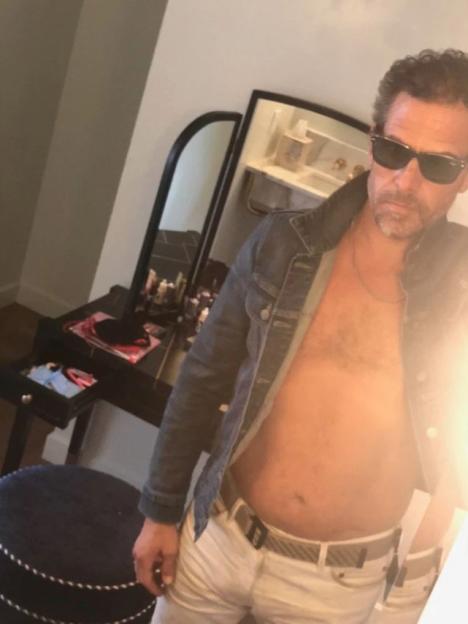 Man in a denim jacket and white pants, shirtless.