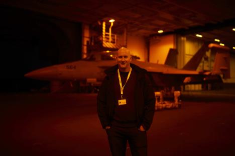Man standing in hangar with fighter jet in background.