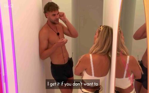 Screenshot of a man and woman talking in a bedroom.