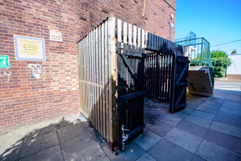 Burned wooden bin enclosure next to a brick building.