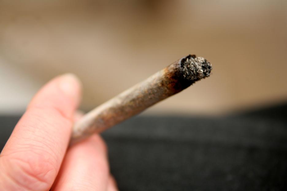 Close-up of a hand holding a lit marijuana cigarette.