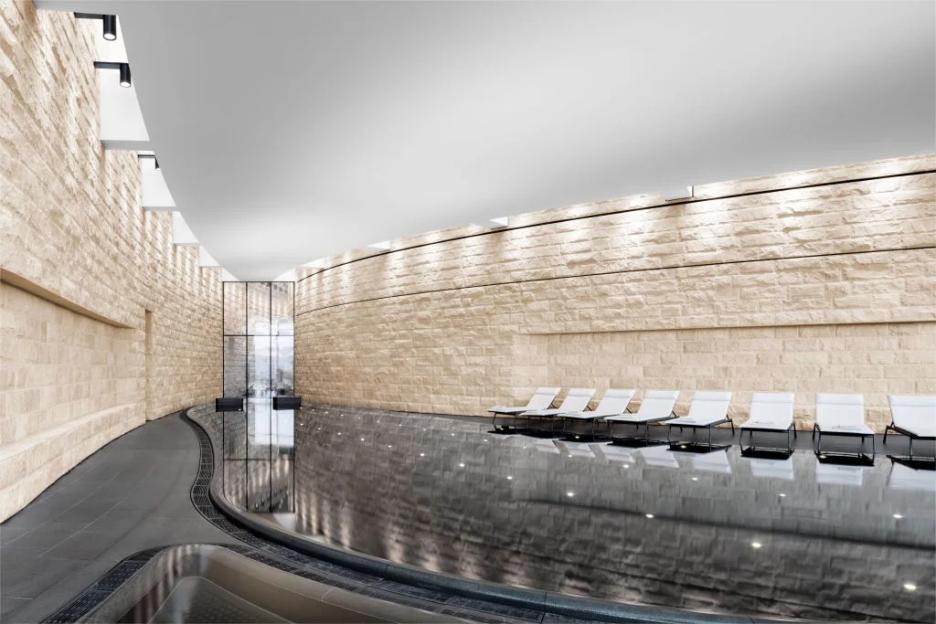 Indoor pool and lounge area with stone walls and white loungers.