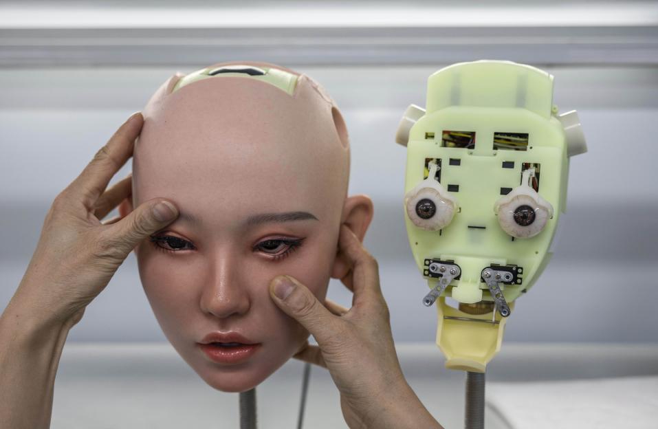 A worker adjusts the silicone skin of a robotic sex doll head in a factory.