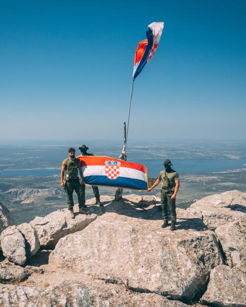 Three soldiers on a mountaintop holding a Croatian flag.