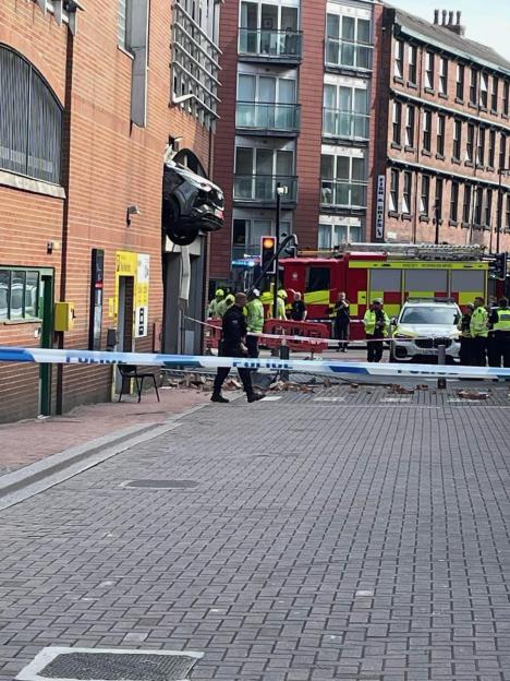 Car crashed through a building, injuring pedestrians; emergency responders at the scene.