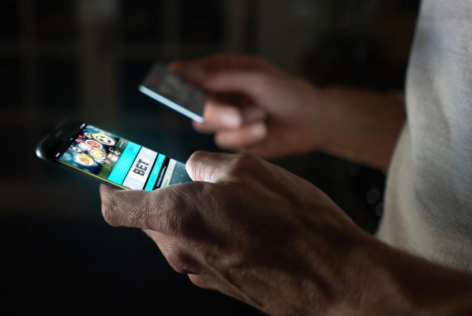 Close-up of a man's hands using a smartphone to place an online bet with a credit card.