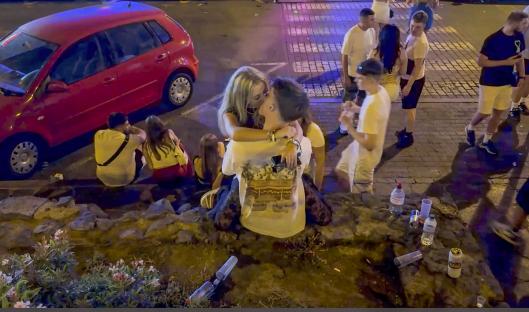 Young people kissing amidst discarded drinks at night.