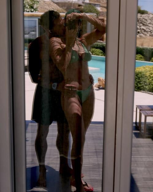Reflection of a couple embracing by a pool, the woman taking a photo.
