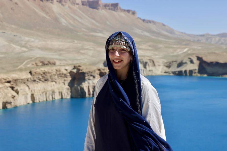 Woman in traditional Afghan clothing smiling in front of a lake.