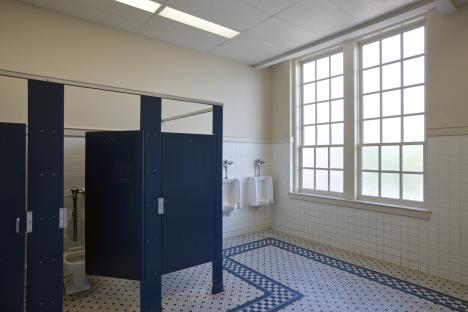Empty school restroom with tiled floor and dark blue stalls.