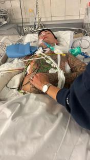 A tattooed man lying in a hospital bed hooked up to medical equipment.