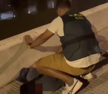 A Guardia Civil officer retrieving an item from the ground.