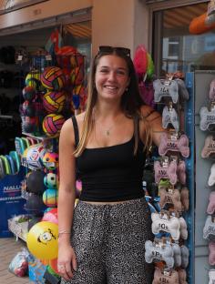 Woman standing in front of a shop selling beach balls and dog toys.