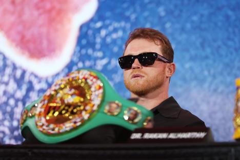 Canelo Ãlvarez at a press conference, wearing sunglasses and holding a championship belt.