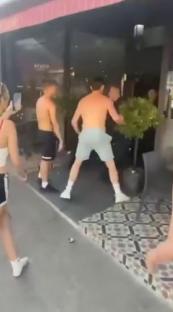 A group of shirtless young men causing a disturbance outside a restaurant.