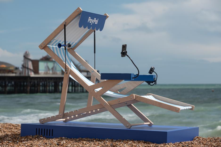 PayPal branded deck chair with phone holder and small fan, on a beach.